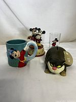 Full view of the four Disney memorabilia items together: mug, music box, glass, and coin bank
