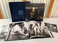 Wide view of the LP album cover, photo book opened to black and white band photo, and 8x10 photo print in front of black commemorative slipcase.