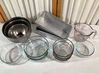 Lots of kitchenware including glass Pyrex bowls, metal loaf pans, stainless steel mixing bowls, and a glass measuring cup.