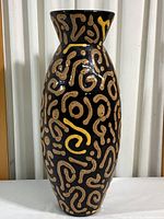 Full front view of the tall black pottery vase showing tan and yellow swirl designs covering the body.