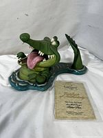 Front and side view of the crocodile figurine showing its details and the certificate of authenticity lying next to it.