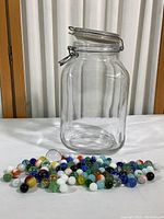 Clear glass jar with glass lid and wire closure, empty, standing on white surface.
