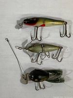 Three wooden fishing lures on a white cloth background showing front and side views.