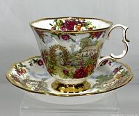 Royal Albert Old Country Roses teacup and saucer angled view showing floral and cottage design and gold accents on the teacup handle and rim.