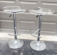 Full view of two chrome swivel stools with clear acrylic seats, showing round bases and attached footrests.
