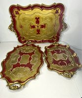 Three Italian Florentine trays in gold and red with ornate designs, all visible with different sizes and patterns
