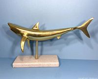 Side view of brass shark sculpture showing polished surface and streamlined form on marble base.