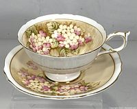 Front angled view of the teacup on the saucer showing detailed pink and white hydrangea flowers with gold rim and handle accents.
