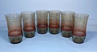 Front view of six mid-century tumblers with tawny brown base and horizontal reddish-brown stripes.