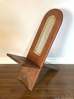 Side angle view of one wooden birthing chair showing intricate carved wooden frame and woven cane panel.