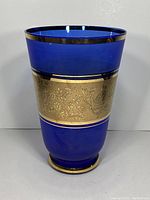 Front view of the cobalt blue glass vase showing gold leaf floral pattern and gold rim.