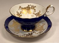 Side angle of tea cup and saucer showing gold floral pattern and gold trim on handle