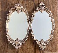 Both mirrors laid flat showing full ornate gold gilt frames and oval reflective surfaces.