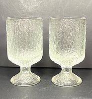 Two vintage Iittala Ultima Thule footed wine glasses standing side by side, showing their textured glass pattern and shape.