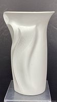 White bisque porcelain vase with flowing ribbed abstract lines and an angular rim, shown from front angle