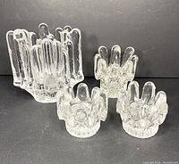 Four clear glass sunflower-shaped candle holders of varying sizes on black background.