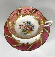 Top down view of teacup and saucer showing pink and gold scroll design and floral bouquet inside cup