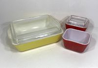 Yellow Pyrex 1.5 quart refrigerator box with clear glass lid, and two red smaller Pyrex refrigerator boxes, one with lid and one without.