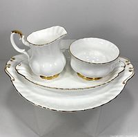 Cream pitcher, sugar bowl, small and large trays arranged on a clear stand showing gold trim and scalloped design