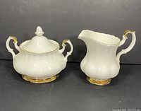 Sugar bowl with lid and creamer jug shown side by side on black background
