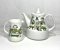Front view of the vintage Turi Market teapot and creamer side by side showing the detailed green and gold human and floral illustrations on white ceramic.