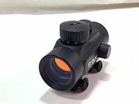 Front view of Tasco Propoint red-dot sight showing large objective lens with orange coating and adjustment dial on top.