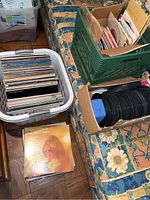 Bins and boxes containing vinyl records and 45s on a floral patterned couch and wooden floor.