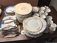 Top view showing stacks of porcelain plates, bowls, cups, and saucers in floral and gold trim designs.
