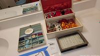Photo showing a wooden framed jewelry box with multiple necklaces including faux pearl strand and an orange bead necklace, alongside a smaller clear box with necklaces.