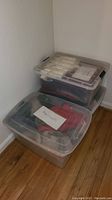 Three translucent plastic bins stacked on the floor. Closest bin holds clothing labeled 'Men's coats'.