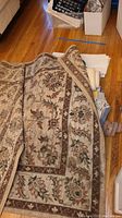 Floral patterned Mohawk Home area rug folded to show top and edges with wood floor background