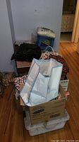 Wide view showing assorted bags and boxes containing sewing and quilting materials stacked on floor.