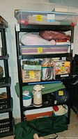 Full view of the black plastic shelving unit with various household items stored on it.