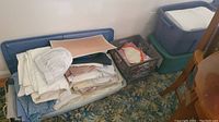 Crate and box filled with folded white and colored linens and napkins, shows quantity and condition