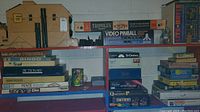 Wide view of shelves containing stacked boxed vintage games including Bingo, Clue, Tripoley, Video Pinball by Atari, Lite-Brite, Tri-Ominos, Simon