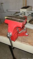 Red Sears metal bench vise bolted to wood table, showing side profile and handle.