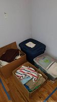 Multiple boxes containing women's tops and blouses, assorted colors and patterns, stacked in a corner