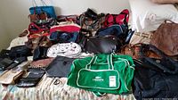 Overview of all bags laid out on a bed, including the Lacoste green duffle bag, assorted purses, handbags, and travel items.