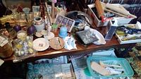 Wide view of assorted kitchen and household items on table including candles, bottles, flatware, rolling pins, and utensils