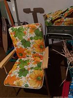 Front angled view of one outdoor folding chair with floral cushioned seat and backrest showing wooden armrests and metal frame.