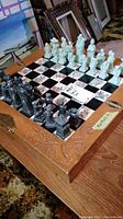 Chess set on table showing full board with tile squares and carved wooden edges, and white and dark composite chess pieces arranged for play.
