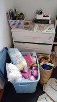 Photo shows blue plastic bin filled with multiple skeins of yarn in pastel colors including white, light yellow, pink, and baby blue, along with other yarn skeins mixed inside.