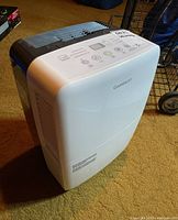 Front and right side view of white Garrison dehumidifier on carpeted floor showing control panel on top and vents.