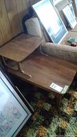 Photo showing two of the vintage wooden end tables placed next to wood-paneled wall and upholstered furniture. Each table has two tiers with tapered legs and a warm wood finish.