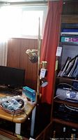 View showing the entire lamp standing next to a desk with a computer monitor. The lamp has three adjustable light fixtures and a black base.