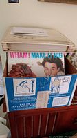 Box filled with multiple LP record albums including a visible Wham! 'Make It Big' album prominently on top.