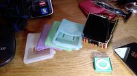 Image of multiple pastel colored iPod and iPad cases stacked alongside a couple of small iPod Nano devices on wooden surface