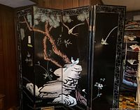 Full view of the six-panel wood screen showing a lacquered black surface with bird, bamboo, and tree motifs.