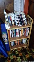 Rattan shelving unit with three shelves filled with books (books not included in the lot). Unit has woven rattan sides and natural light wood color.