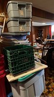 Stack of plastic storage bins with lids and green crate on top